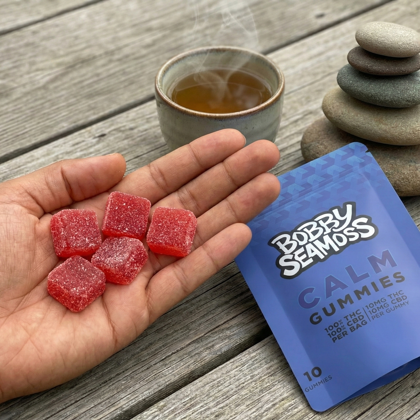 Hand holding red gummy bears next to a blue 'Bodhi Seamus' gummy bear package on a wooden surface.